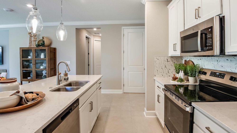 A modern kitchen features white cabinets, a quartz island with a sink, and stainless appliances — 25 GEOSAM DRIVE, PALM COAST, FL