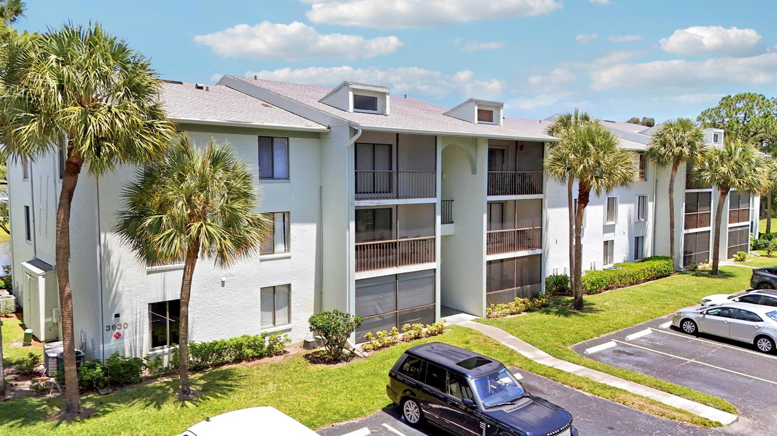An exterior view of a three-story apartment building with palm trees and a parking lot — 3630 Alder Drive # E2, West Palm Beach FL 33417, WEST PALM BEACH, FL