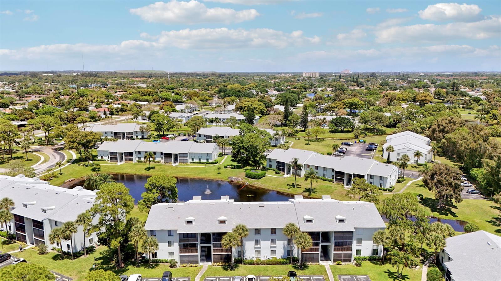 Aerial view of multi-story apartment buildings surrounding a central pond in a landscaped residential area — 3630 Alder Drive # E2, West Palm Beach FL 33417, WEST PALM BEACH, FL