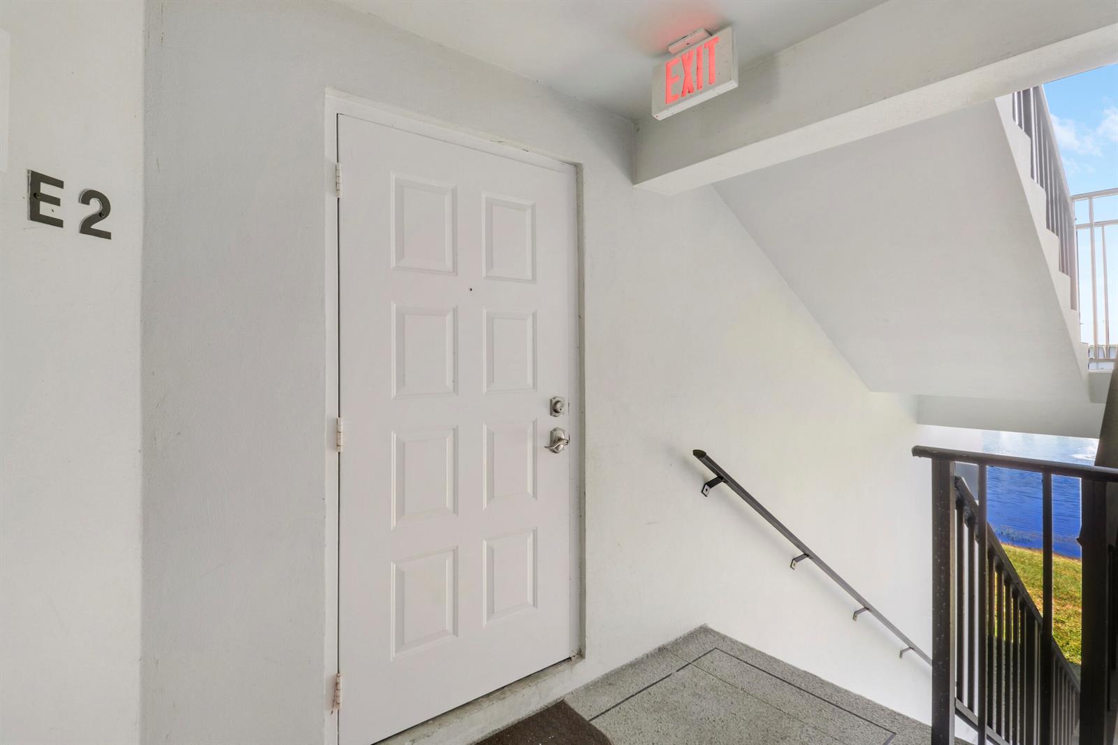 A white apartment door labeled E2 is located next to an outdoor stairwell — 3630 Alder Drive # E2, West Palm Beach FL 33417, WEST PALM BEACH, FL