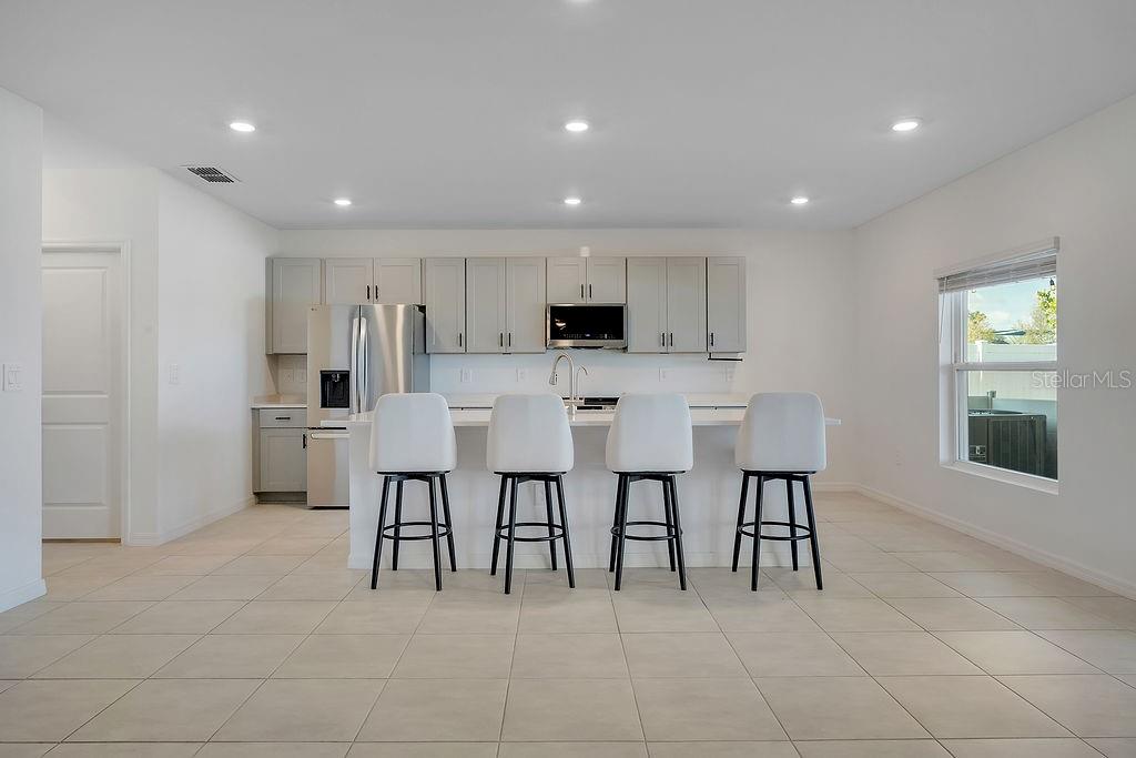 An open-concept kitchen features white cabinetry, stainless steel appliances, and a breakfast bar with stools — 1033 CALICO POINTE CIRCLE, GROVELAND, FL