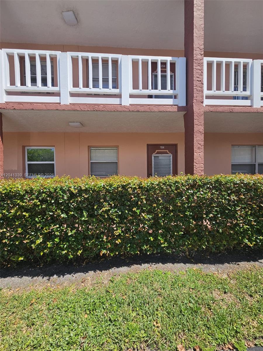 A two-story apartment building exterior features a ground-level unit with a hedge in front — SUNRISE, FL