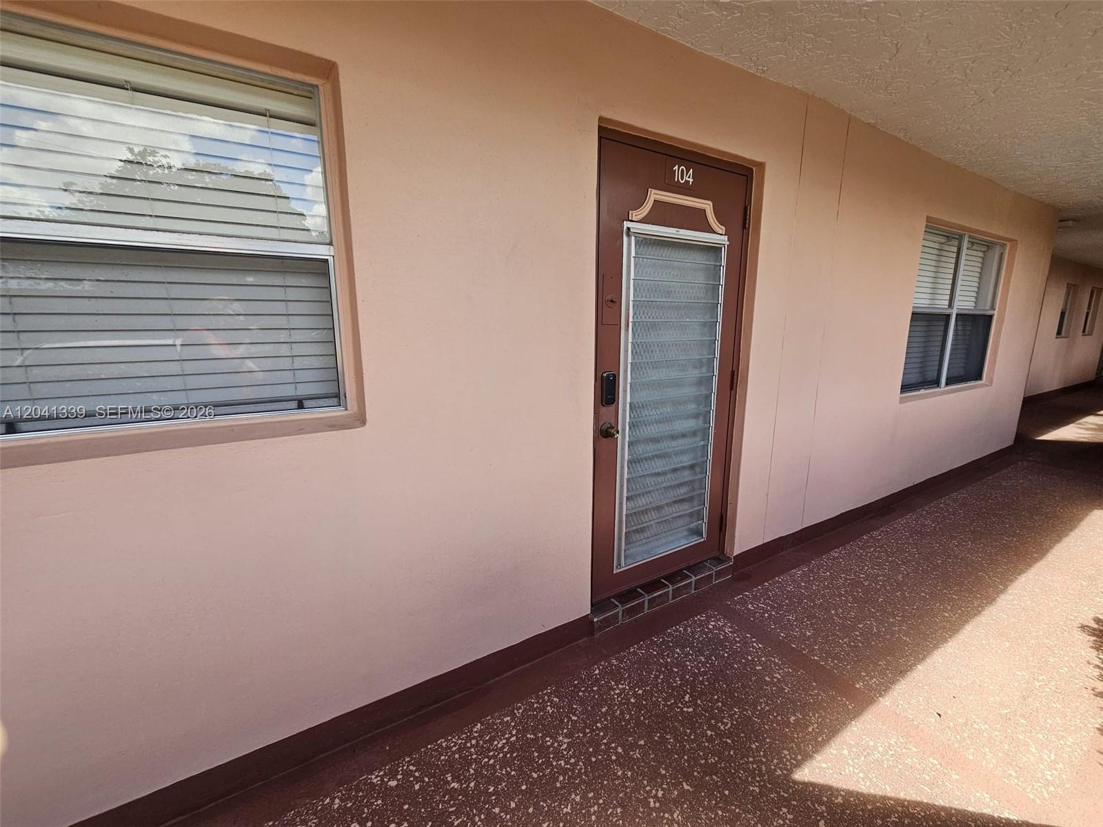 The exterior of a residential unit features a brown door numbered 104 and windows — SUNRISE, FL