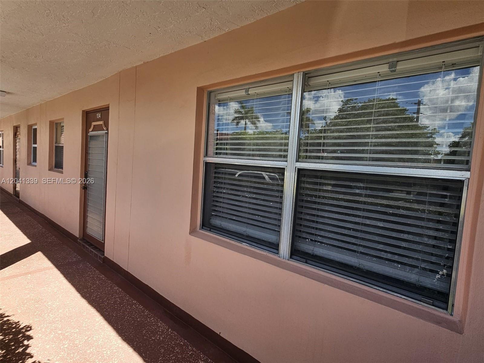 An exterior view of a peach-colored building with a walkway, windows, and a door — SUNRISE, FL
