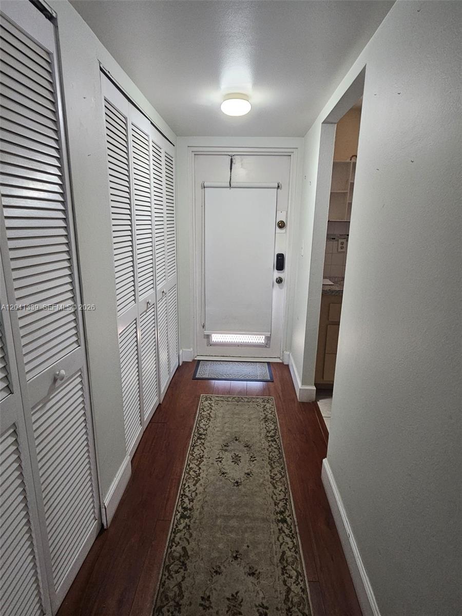 A hallway features wood-look flooring, a runner rug, louvered closet doors, and a white entry door — SUNRISE, FL