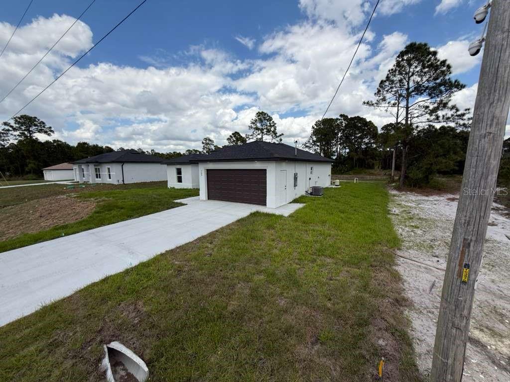 A white single-story house with a dark roof and garage sits on a grassy lot — 765 PUCCINI AVE S, LEHIGH ACRES, FL
