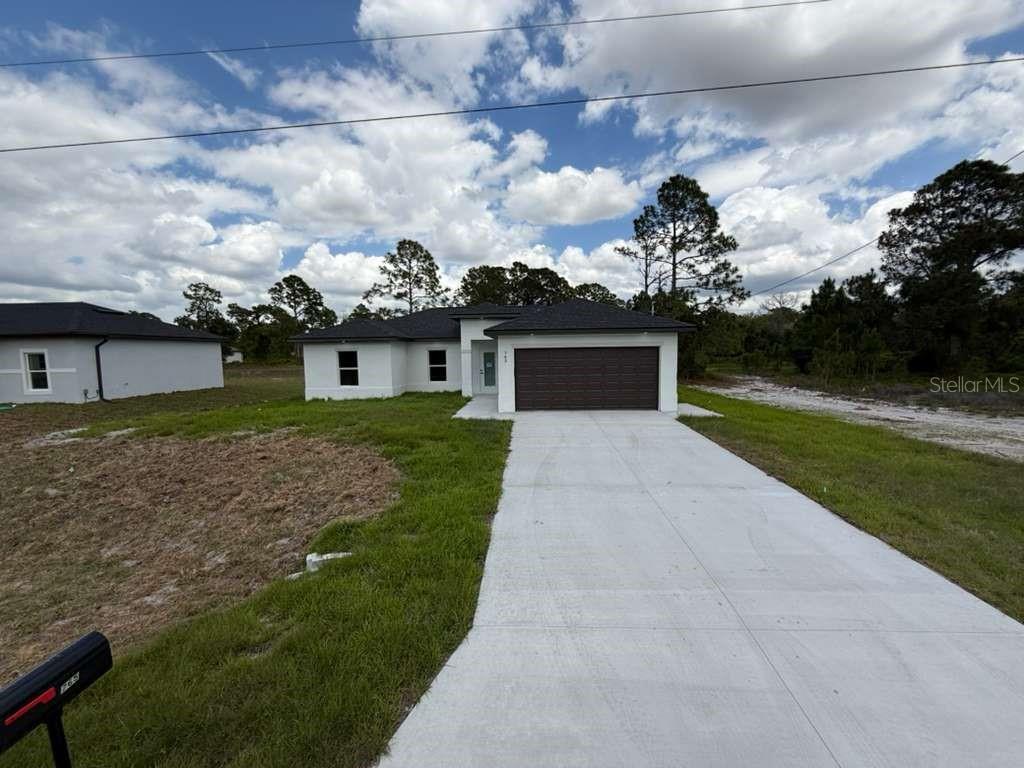 A newly constructed single-story house with a white exterior, dark roof, and concrete driveway — 765 PUCCINI AVE S, LEHIGH ACRES, FL