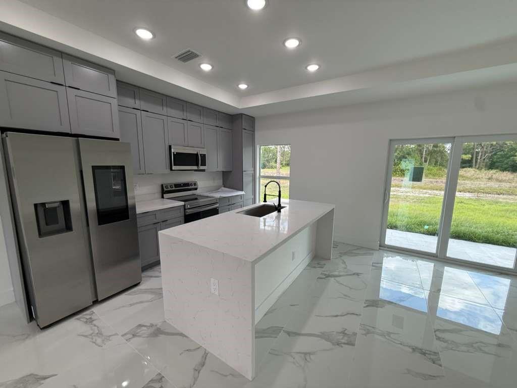 A modern kitchen features gray cabinetry, a white quartz island, and marble-look tile flooring — 765 PUCCINI AVE S, LEHIGH ACRES, FL