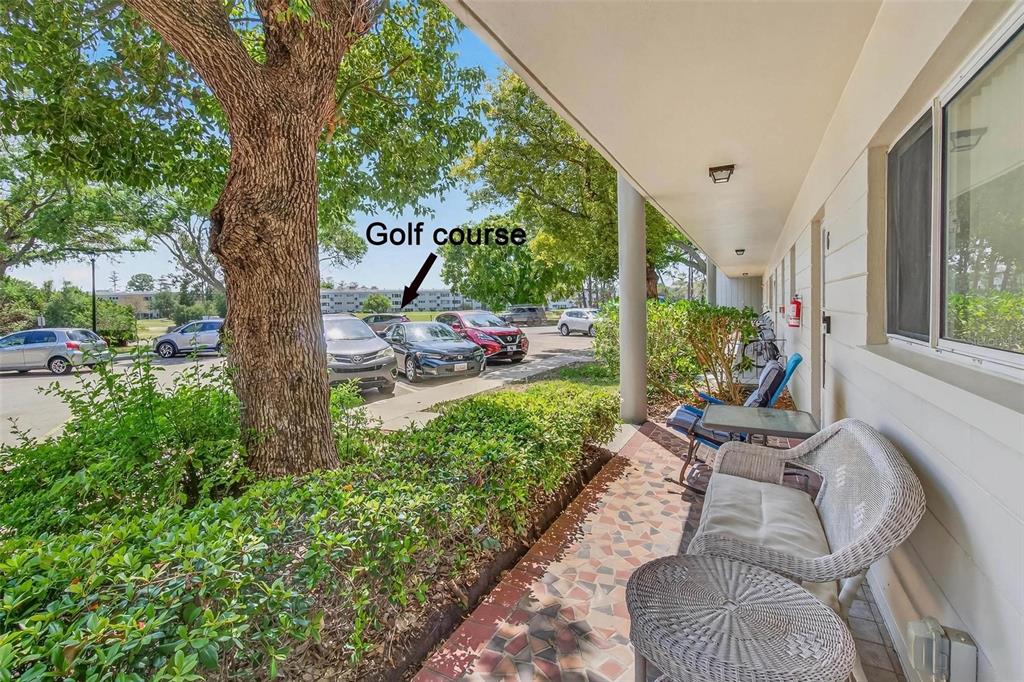 A covered patio with wicker furniture overlooks a parking lot and a golf course — 2440 WORLD PARKWAY BOULEVARD UNIT 6, CLEARWATER, FL