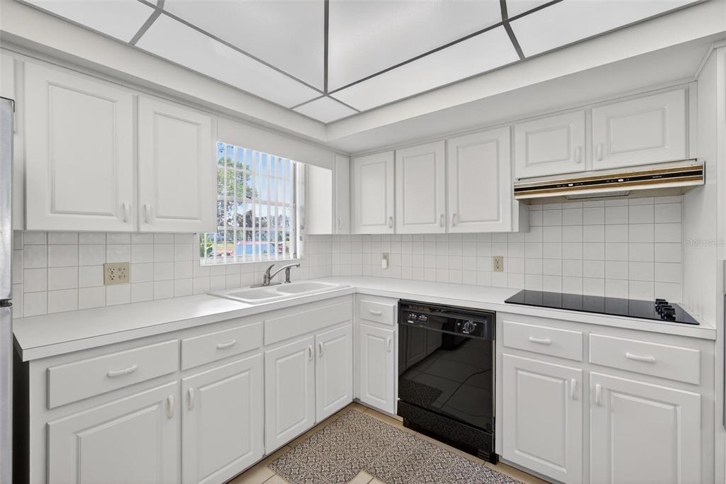 A kitchen with white cabinets, white tile backsplash, black appliances, and a grid ceiling light — 2440 WORLD PARKWAY BOULEVARD UNIT 6, CLEARWATER, FL