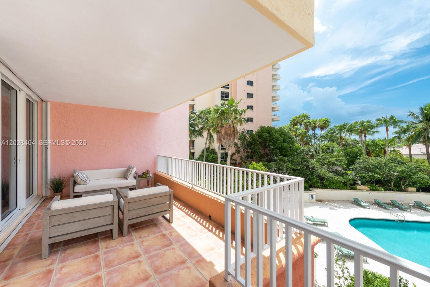 A balcony with terracotta tile flooring features outdoor seating overlooking a pool and palm trees — 781 Crandon Blvd # 405, Key Biscayne FL 33149, KEY BISCAYNE, FL