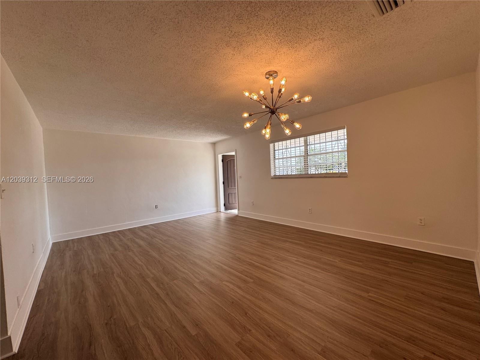 An empty room features light wood-look flooring, white walls, and a modern sputnik chandelier — 3632 SW 87th Ave, Miami FL 33165, MIAMI, FL
