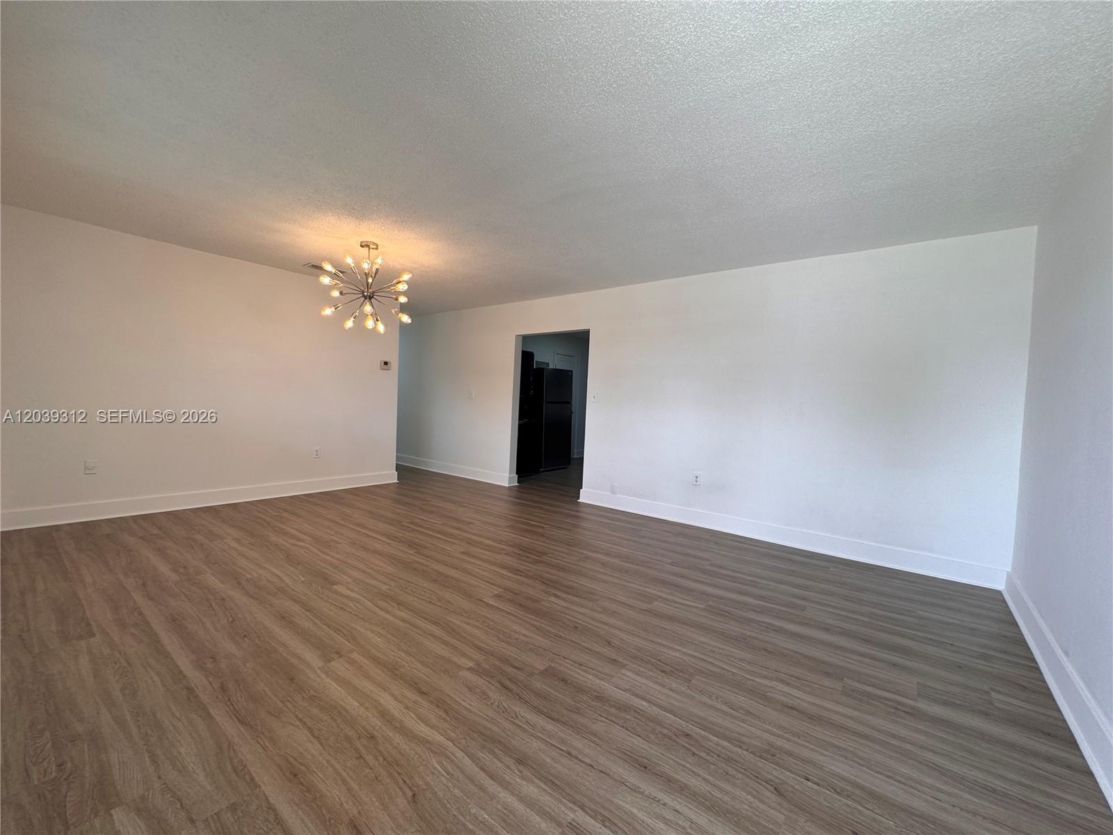 An empty room features white walls, wood-look flooring, and a modern sputnik-style light fixture — 3632 SW 87th Ave, Miami FL 33165, MIAMI, FL