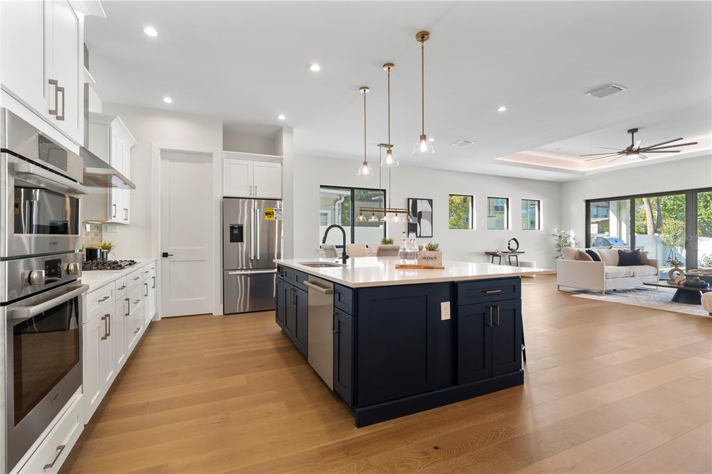 A modern kitchen features a dark blue island, white cabinetry, stainless steel appliances, and hardwood floors — 1606 MILLER AVENUE, WINTER PARK, FL