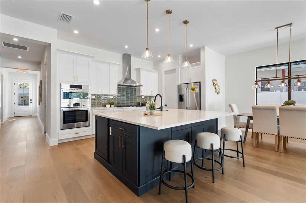A modern kitchen features a dark blue island, white cabinetry, stainless steel appliances, and wood flooring — 1606 MILLER AVENUE, WINTER PARK, FL