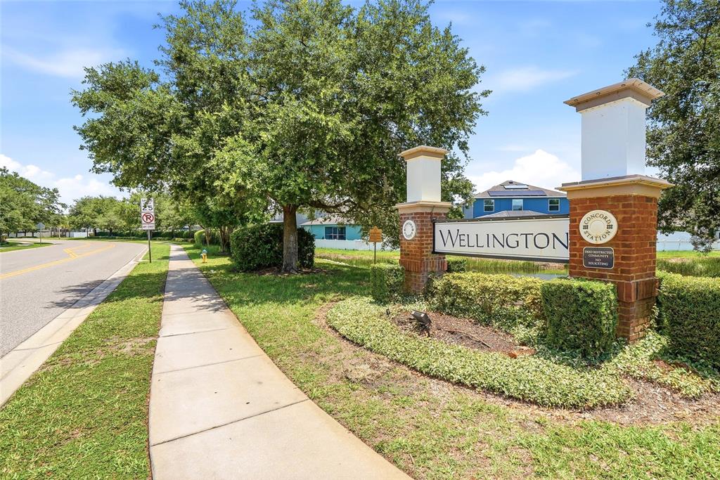 A brick monument sign for Wellington at Concord Station stands beside a sidewalk and road — 3987 ROUND TABLE COURT, LAND O LAKES, FL