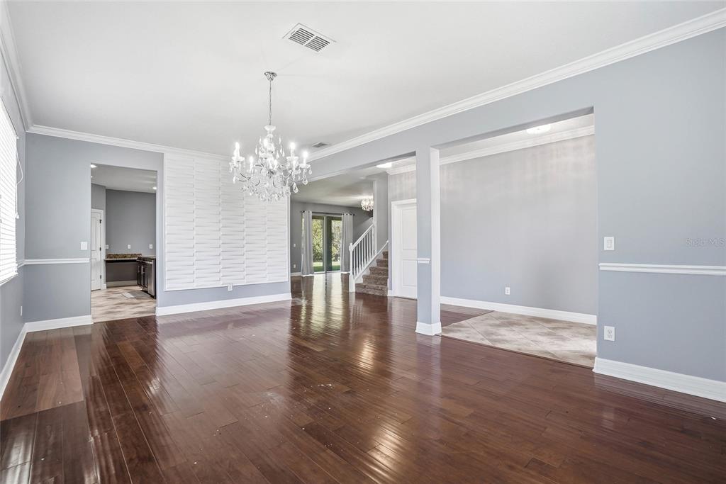 An open living area features dark hardwood floors, a crystal chandelier, and a white accent wall — 3987 ROUND TABLE COURT, LAND O LAKES, FL