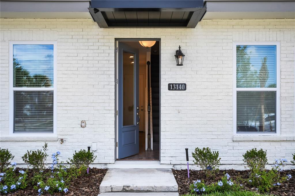 The exterior of a white brick house features a blue front door and two windows — 13140 BOVET AVENUE, ORLANDO, FL