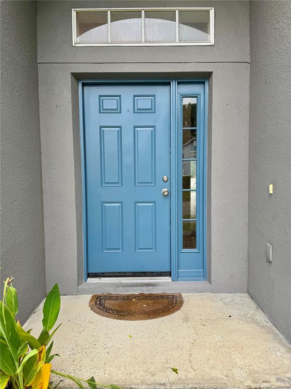 A blue front door with a side window and transom window set in a gray wall — 14605 KRISTENRIGHT LANE, ORLANDO, FL