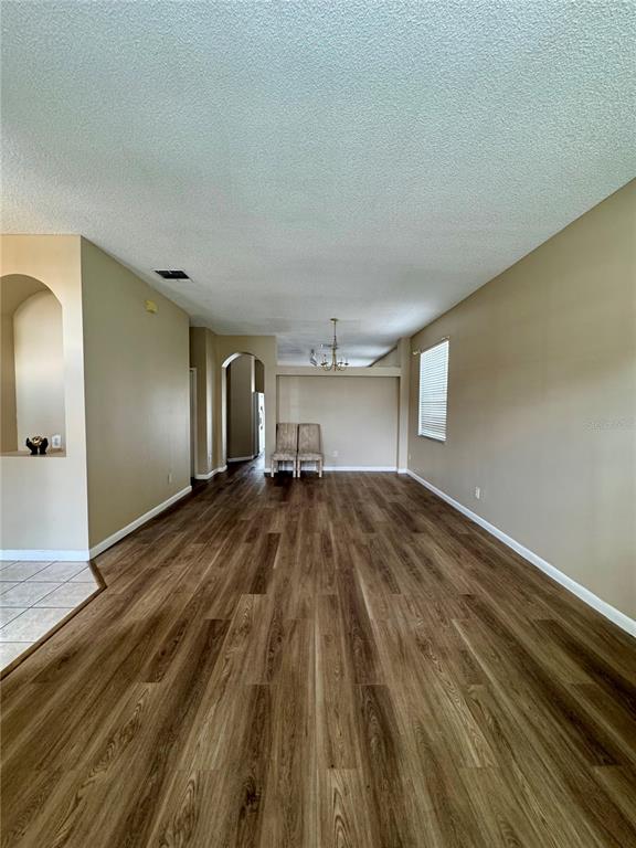 A spacious room with wood-look flooring, beige walls, and an arched entryway — 14605 KRISTENRIGHT LANE, ORLANDO, FL