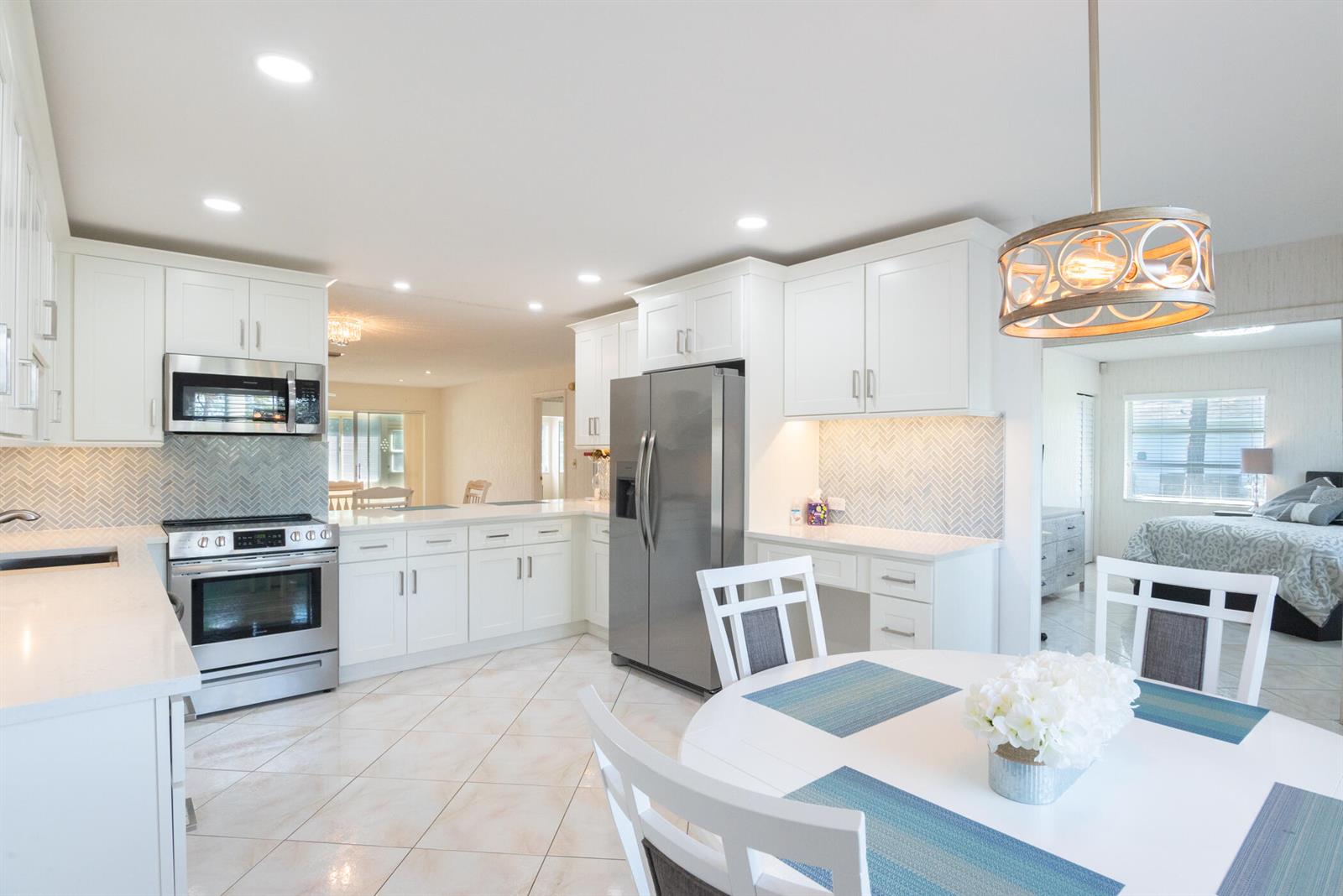 A bright kitchen features white cabinets, stainless steel appliances, and a round dining table — 5160 Petal Place # D, Delray Beach FL 33484, DELRAY BEACH, FL