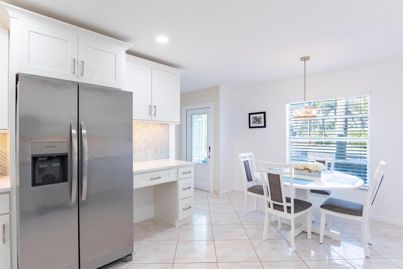 A kitchen features white cabinets, stainless steel appliances, a built-in desk, and a dining area — 5160 Petal Place # D, Delray Beach FL 33484, DELRAY BEACH, FL