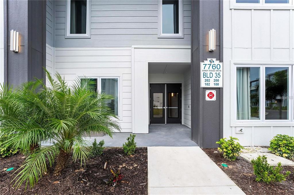 The exterior entrance of a multi-unit residential building features a concrete walkway and landscaping — 7760 SANDY RIDGE DRIVE UNIT 202, REUNION, FL
