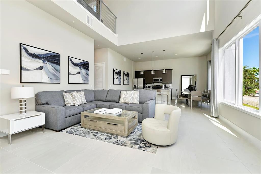 A modern living room with a grey sectional sofa, coffee table, and open kitchen area — 7760 SANDY RIDGE DRIVE UNIT 202, REUNION, FL