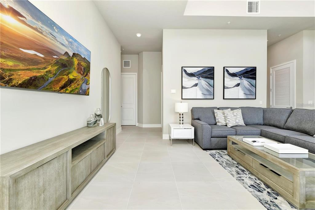A living room features a wall-mounted television, a gray sectional sofa, and light tile flooring — 7760 SANDY RIDGE DRIVE UNIT 202, REUNION, FL