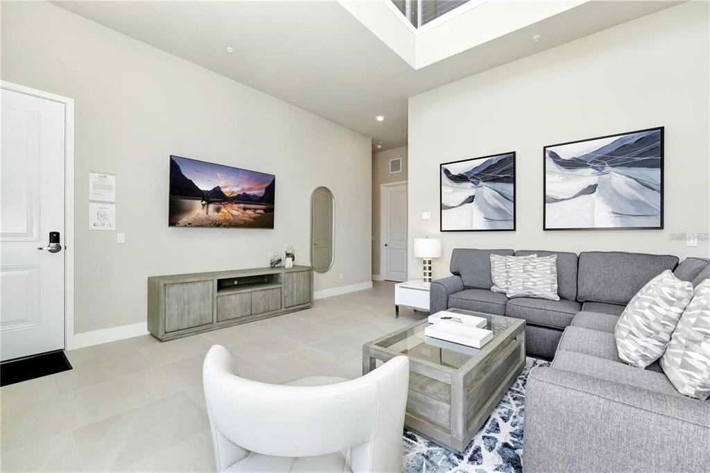 A living room features a grey sectional sofa, a glass coffee table, and a wall-mounted television — 7760 SANDY RIDGE DRIVE UNIT 202, REUNION, FL