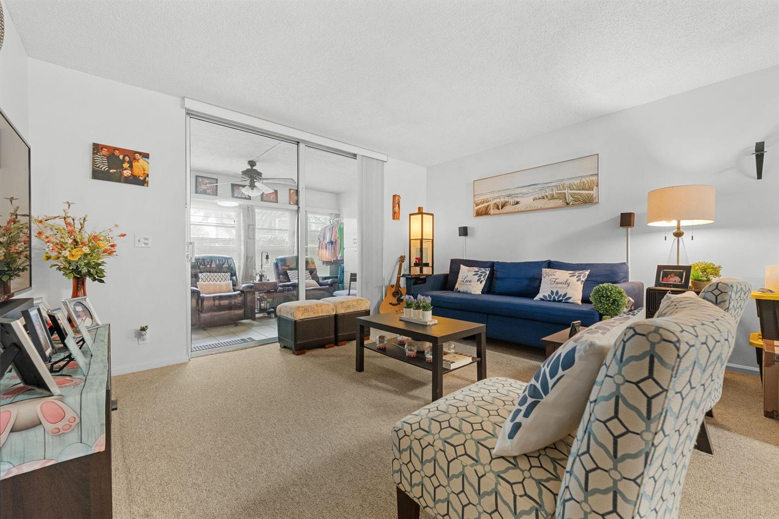 A living room with a blue sofa, patterned accent chair, and sliding glass doors — 14527 Bonaire Boulevard # 109, Delray Beach FL 33446, DELRAY BEACH, FL