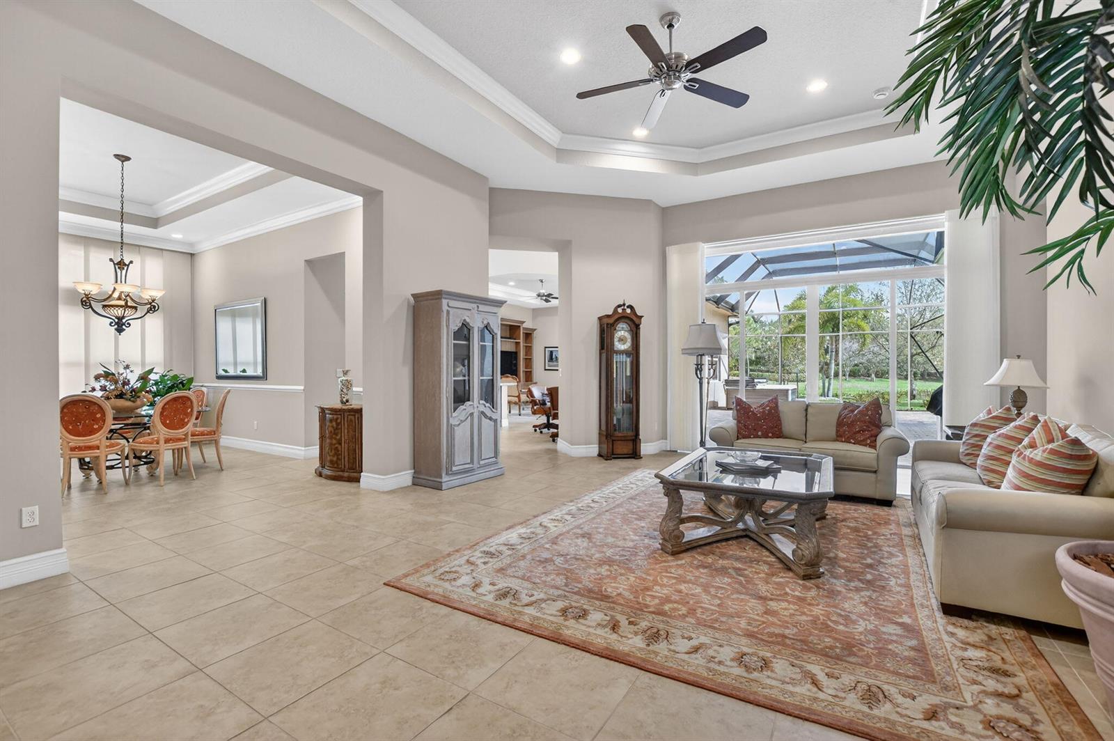 A living room with tile floors, a tray ceiling, and a view of a pool cage — 12133 Glacier Bay Drive, Boynton Beach FL 33473, BOYNTON BEACH, FL