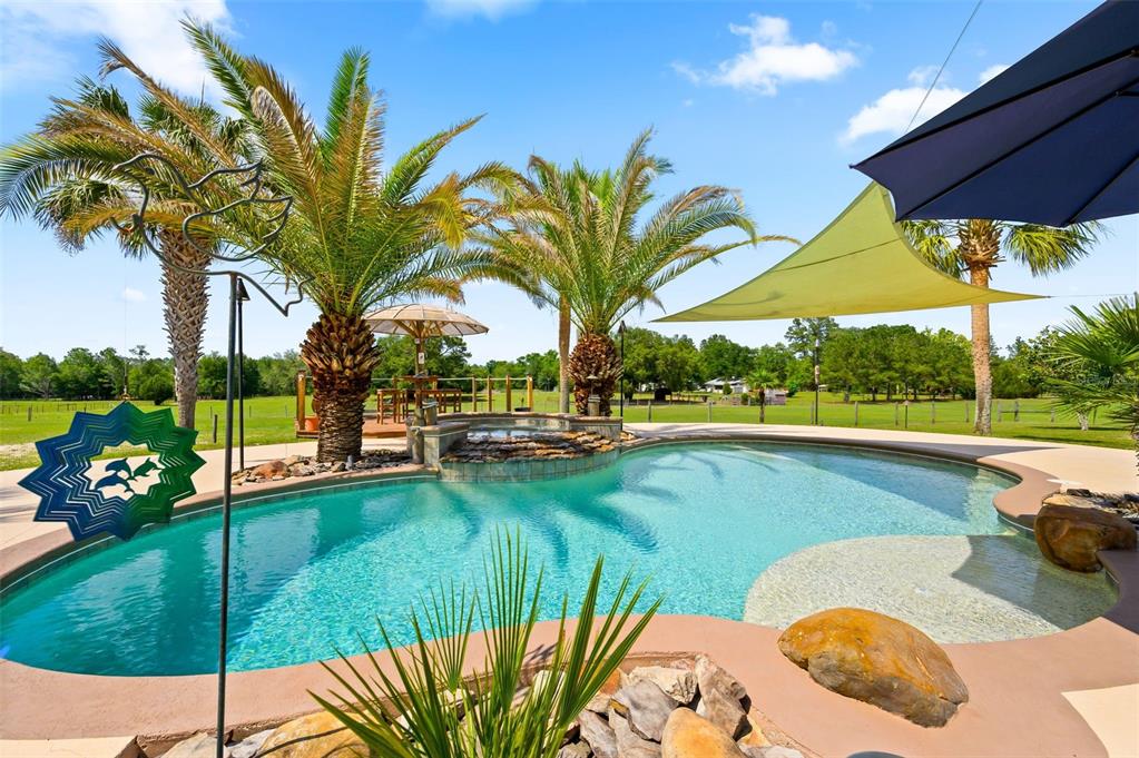 A backyard swimming pool with a rock waterfall, palm trees, and shade sails — 6739 SE 67TH COURT, TRENTON, FL