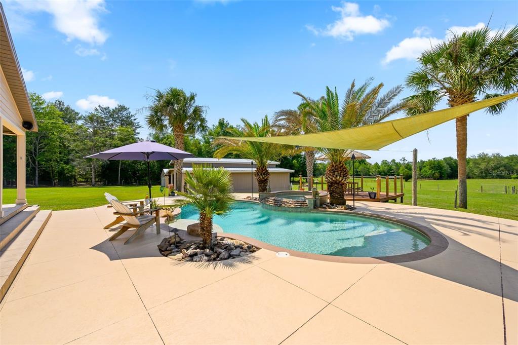 A backyard features a swimming pool with a hot tub, palm trees, and a shade sail — 6739 SE 67TH COURT, TRENTON, FL
