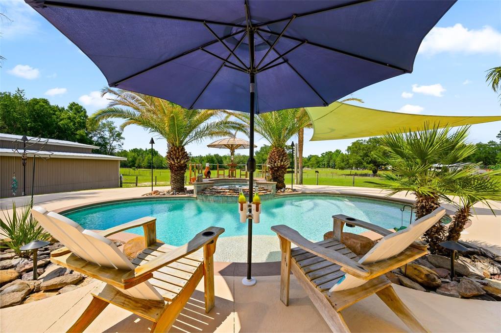 A swimming pool with a hot tub, lounge chairs, and umbrellas in a backyard setting — 6739 SE 67TH COURT, TRENTON, FL