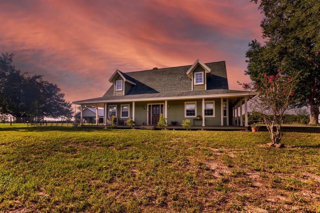 A two-story green farmhouse with a wrap-around porch stands on a grassy lot at sunset — 24948 WALKABOUT RANCH ROAD, SORRENTO, FL