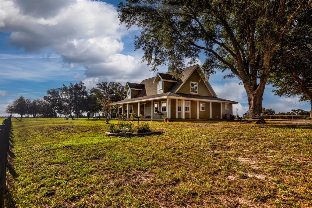 A two-story house with a wrap-around porch sits on a grassy lot under trees — 24948 WALKABOUT RANCH ROAD, SORRENTO, FL