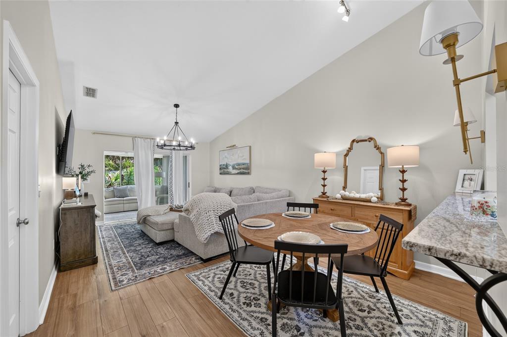 An open-concept living and dining area features vaulted ceilings, wood-look flooring, and a sliding door — 2429 SE 18TH CIRCLE, OCALA, FL