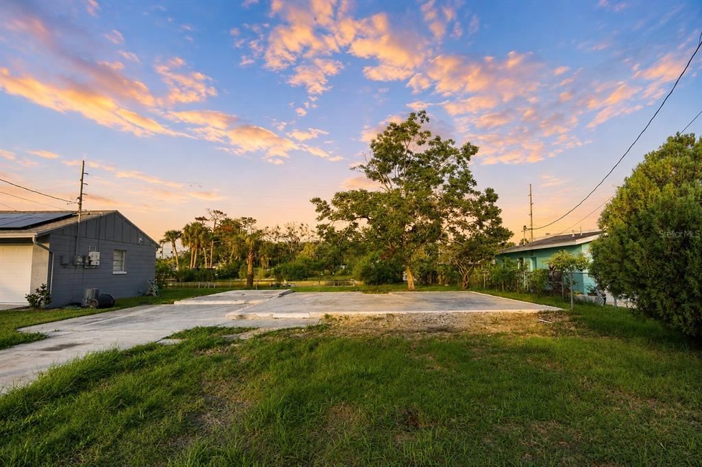 A concrete slab foundation sits in a grassy yard between two residential houses at sunset — 13900 MURIEL AVENUE, HUDSON, FL
