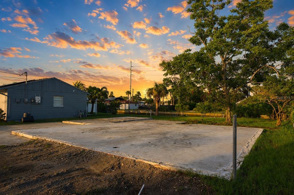 A concrete slab foundation sits in a grassy yard next to a gray house — 13900 MURIEL AVENUE, HUDSON, FL