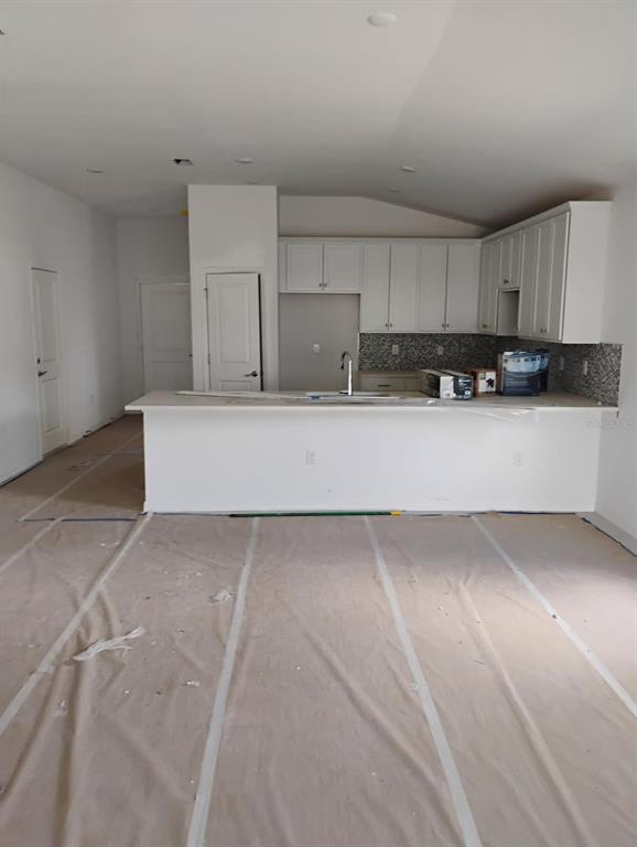 An unfinished kitchen features white cabinets, a central island, and protective paper covering the floor — 3430 SARTO LANE, ROTONDA WEST, FL