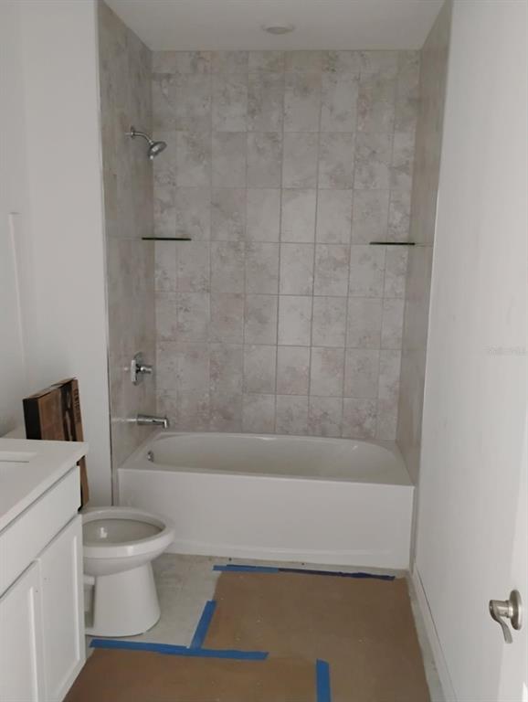 A bathroom features a white bathtub with a tiled surround, a toilet, and a vanity — 3430 SARTO LANE, ROTONDA WEST, FL
