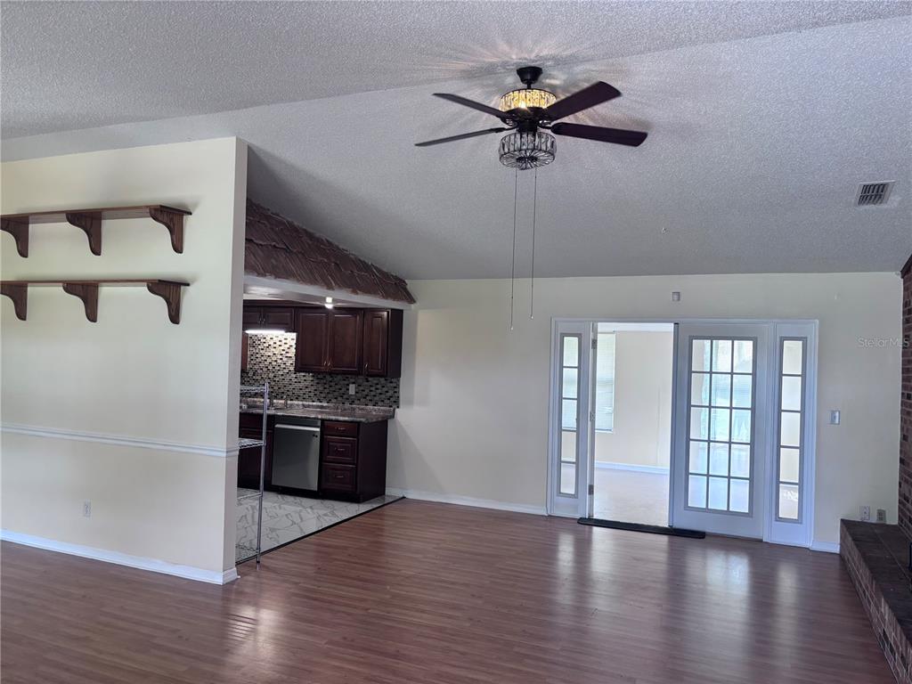 A living room with wood-look flooring, a ceiling fan, and an adjacent kitchen with dark cabinets — 4907 NE 6TH STREET, OCALA, FL