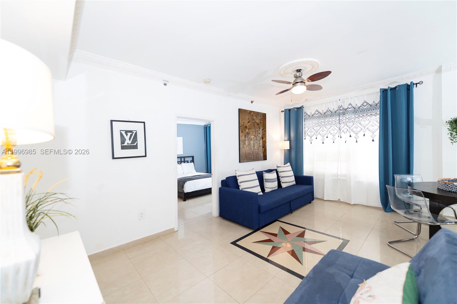 A living room features a blue sofa, tiled floors, a ceiling fan, and a bedroom doorway — 918 Ocean Dr # 202, Miami Beach FL 33139, MIAMI BEACH, FL