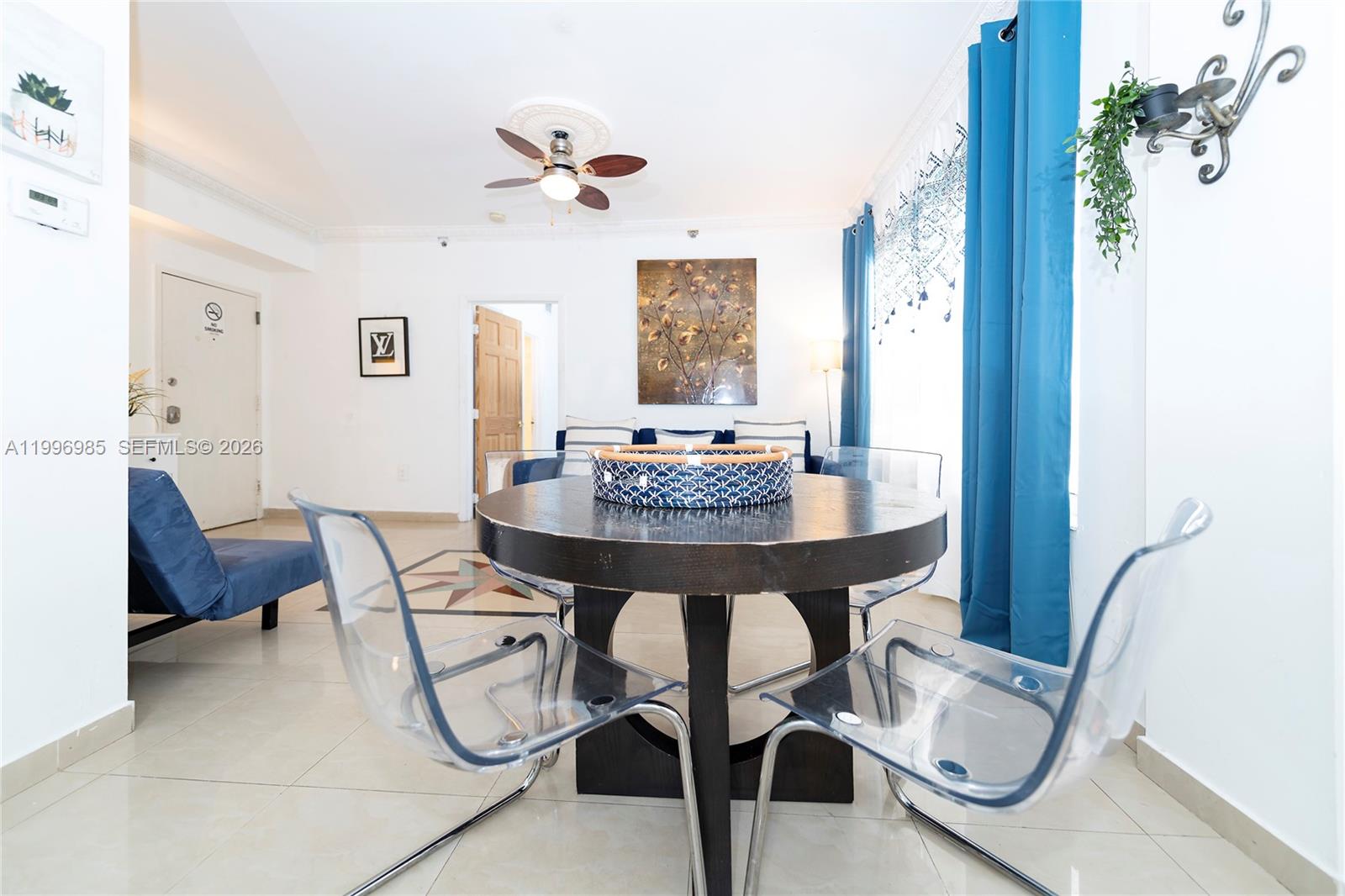 A dining area features a round dark wood table, clear chairs, and blue curtains — 918 Ocean Dr # 202, Miami Beach FL 33139, MIAMI BEACH, FL