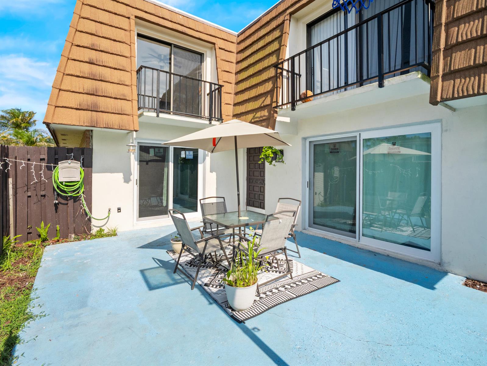 A patio with a dining set and umbrella sits outside a two-story building with balconies — 1814 Kaileen Circle NE, Palm Bay FL 32905, PALM BAY, FL