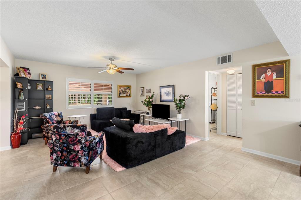 A living room features tile flooring, a ceiling fan, and a mix of floral and black furniture — 275 INDIGO DRIVE UNIT 104, DAYTONA BEACH, FL