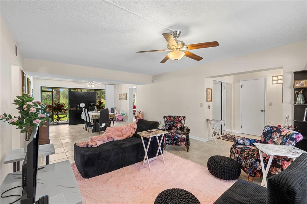 A living room features a pink rug, black furniture, floral armchairs, and a ceiling fan — 275 INDIGO DRIVE UNIT 104, DAYTONA BEACH, FL