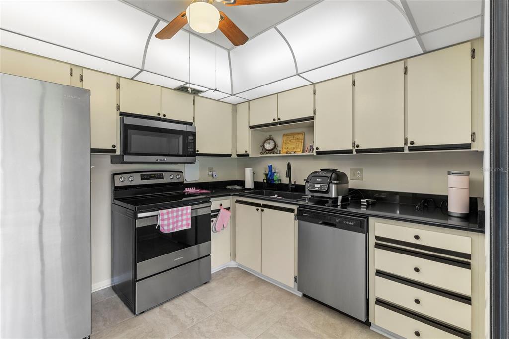 A kitchen features light-colored cabinets, stainless steel appliances, black countertops, and a ceiling fan — 275 INDIGO DRIVE UNIT 104, DAYTONA BEACH, FL