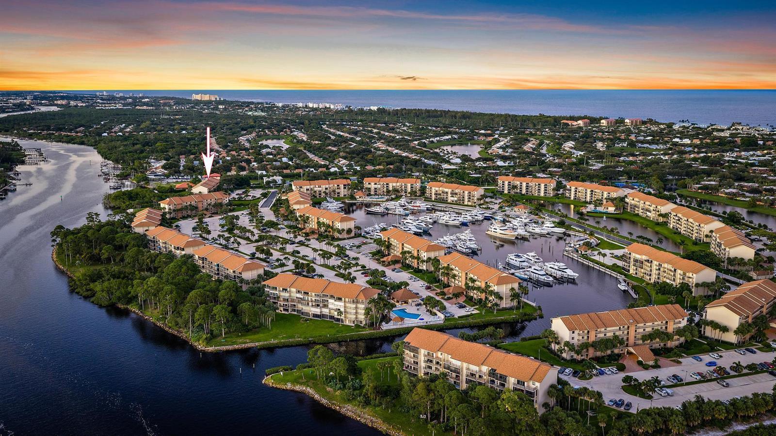 An aerial view shows a waterfront condominium complex with a marina and a sunset sky — 1701 Marina Isle Way # 202, Jupiter FL 33477, JUPITER, FL